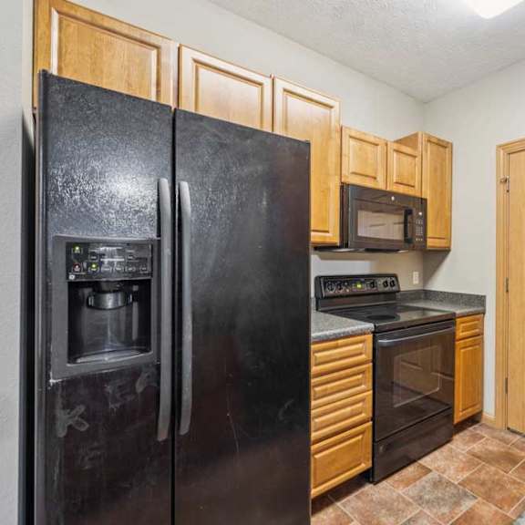 Thumbnail 5 of 20 Kitchen with black refrigerator, oven, and over-the-range microwave, wood cabinetry, and a pantry closet door for extra storage.