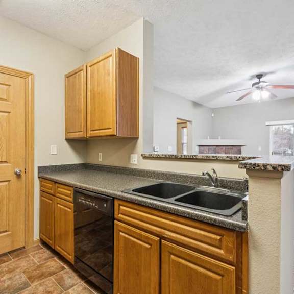 Thumbnail 8 of 20 Kitchen with double-basin sink, black dishwasher, raised breakfast bar, and open view into the living room with fireplace and balcony access.