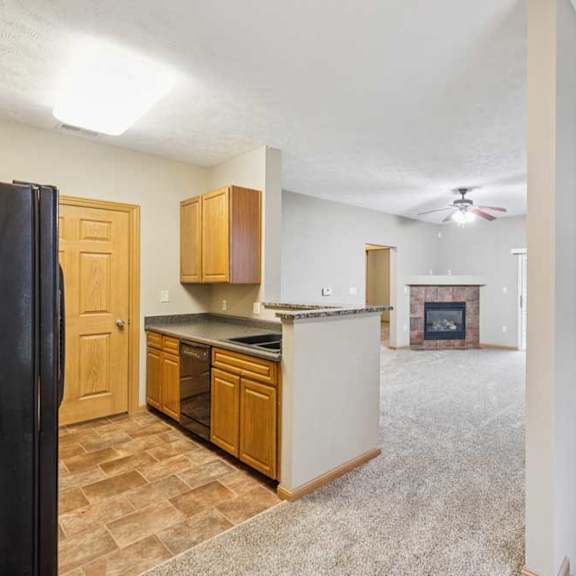 Thumbnail 3 of 20 Open-concept apartment layout featuring kitchen with breakfast bar, carpeted living room, corner fireplace, and stairwell railing detail.