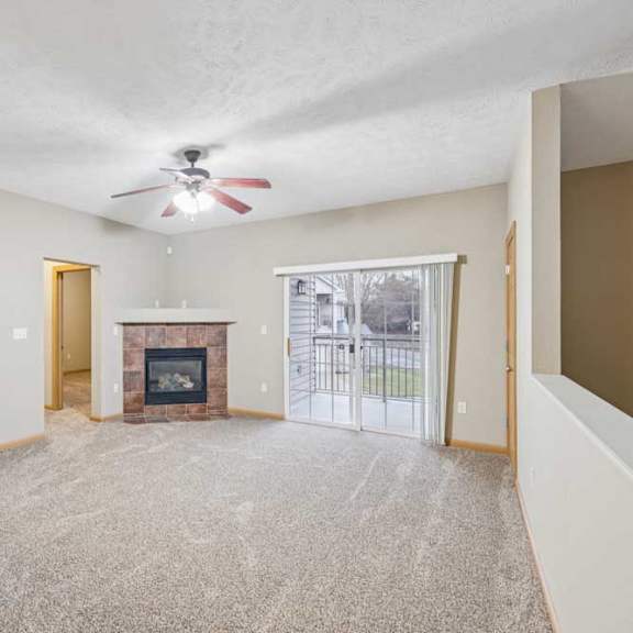 Thumbnail 10 of 20 Spacious living room with ceiling fan, corner tile-surround fireplace, and sliding glass door leading to a private balcony.
