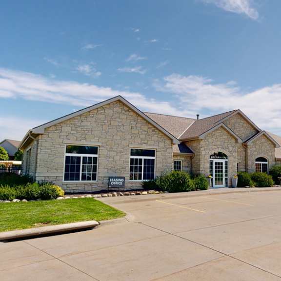 an apartment clubhouse exterior with a stone facade and a car parked in front.
