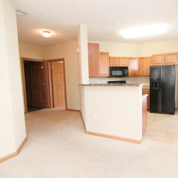 Thumbnail 4 of 12 an empty living room with a kitchen with black appliances