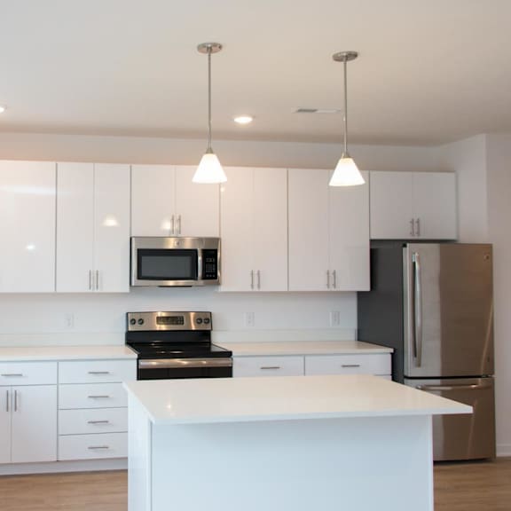 Thumbnail 3 of 8 A large L-shaped kitchen with an island. cabinets and counters are white with stainless steel appliances