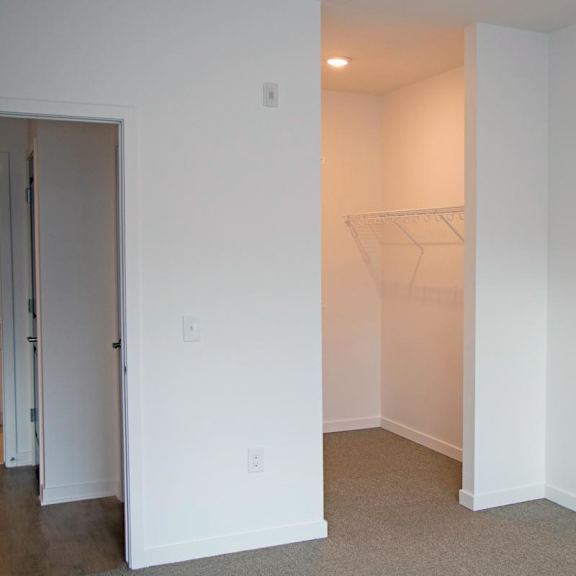 Thumbnail 7 of 8 A white room with a doorway leading to another an empty walk-in closet