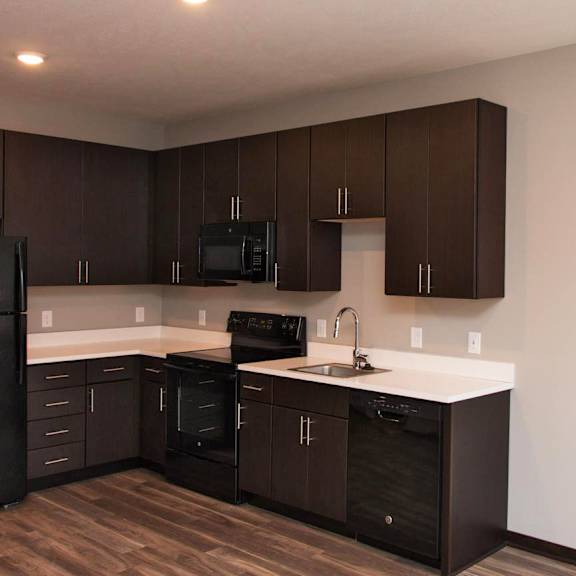 Thumbnail 5 of 6 A kitchen with dark brown cabinets and a black refrigerator.