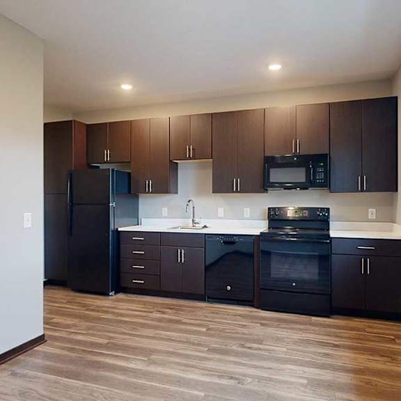 Thumbnail 5 of 17 A kitchen with dark wood cabinets next to a living area with hardwood floors and a large window