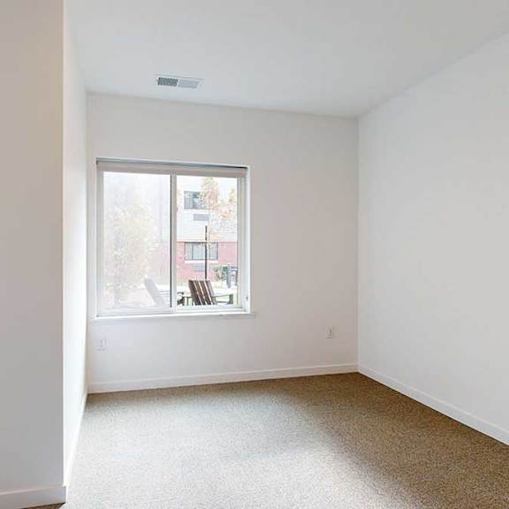 Thumbnail 9 of 28 a bedroom with a large window looking out to the courtyard and carpet flooring