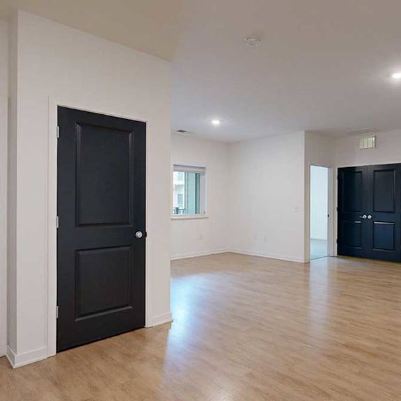 Thumbnail 21 of 28 a living room with light walls and dark doors to closets and bedrooms with hardwood floors
