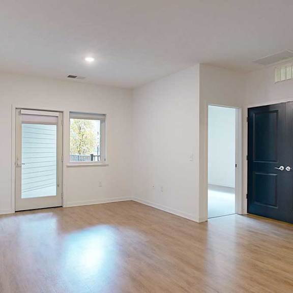Thumbnail 7 of 28 a living room with balcony access and doors to a bedroom and the laundry room