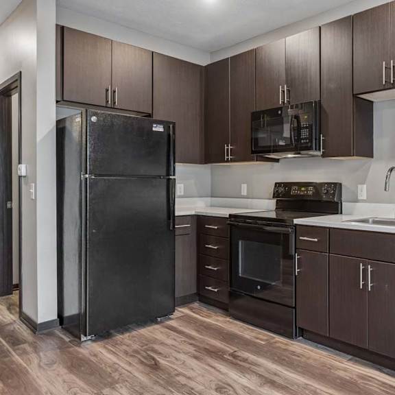Thumbnail 2 of 15 Contemporary apartment kitchen with dark wood cabinetry, black appliances, white countertops, and a functional U-shaped layout.