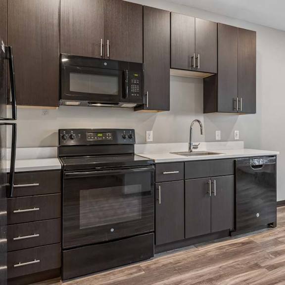 Thumbnail 3 of 15 Stylish apartment kitchen with dark wood cabinetry, black appliances, white countertops, and an open dining area.