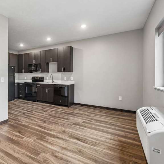Thumbnail 5 of 15 Open studio apartment with wood-style flooring, a compact kitchen, recessed lighting, and a bright, open living area.