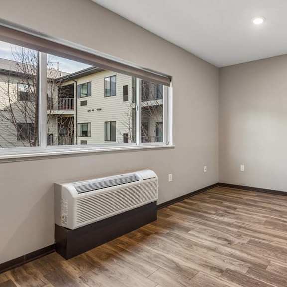 Thumbnail 7 of 15 Bright studio apartment living area with wood-style flooring, a large window, and abundant natural light.