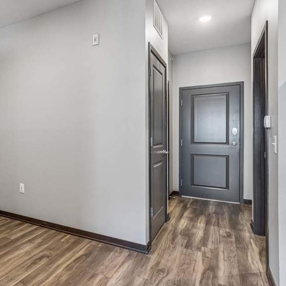 Thumbnail 10 of 15 Studio apartment alcove with wood-style flooring, neutral finishes, and an open hallway leading to the entry and kitchen.