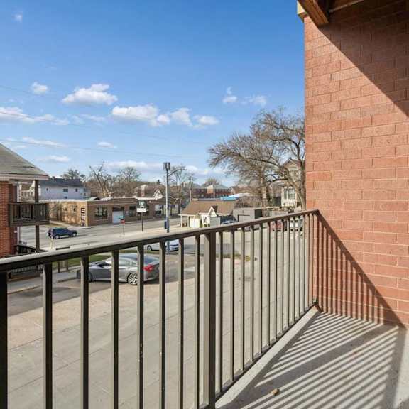 Thumbnail 34 of 34 Private apartment balcony with a black metal railing, brick exterior, and neighborhood views under a clear blue sky.