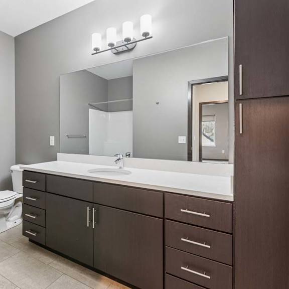 Thumbnail 31 of 34 Modern apartment bathroom with a double-sink vanity, dark wood cabinetry, a large mirror, and bright vanity lighting.