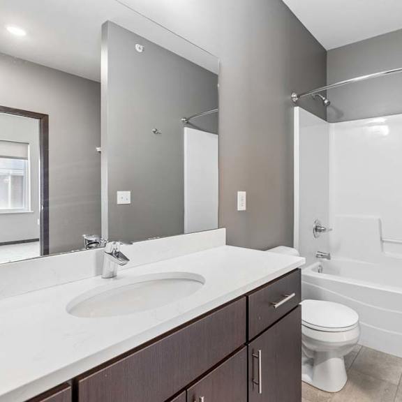 Thumbnail 32 of 34 Bright apartment bathroom with a single-sink vanity, large mirror, and a tub and shower combination with neutral finishes.