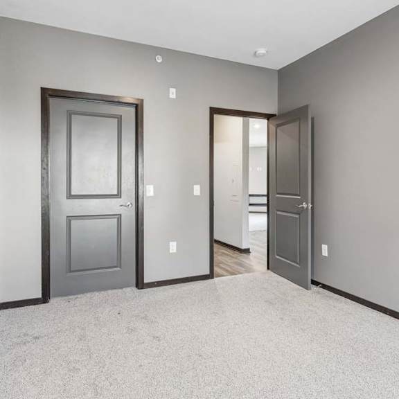 Thumbnail 25 of 34 Carpeted apartment bedroom with gray walls, double-door closet access, and an open doorway leading to the hallway.