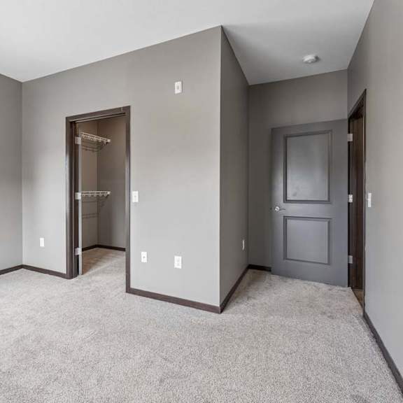 Thumbnail 29 of 34 Spacious apartment bedroom with soft carpeting, a large window, walk-in closet access, and gray walls.