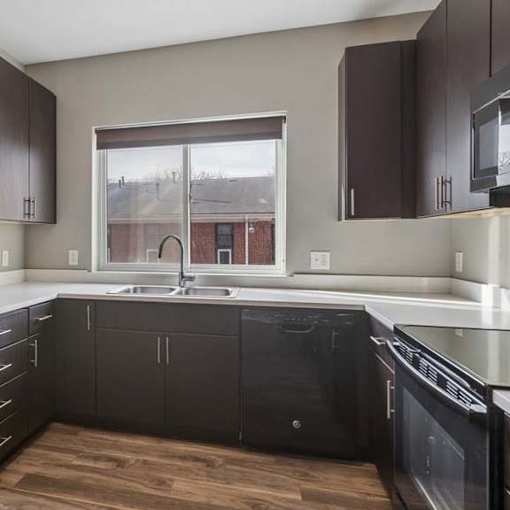 Thumbnail 19 of 34 Contemporary apartment kitchen with dark wood cabinetry, quartz-style countertops, a large window, and an L-shaped layout.