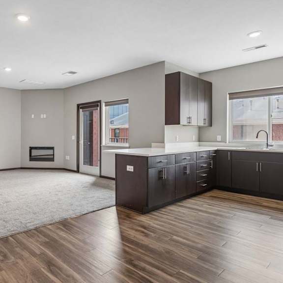 Thumbnail 22 of 34 Open-concept apartment living area with plush carpeting, wood-style flooring, a modern kitchen, and a sliding glass door to a private patio.