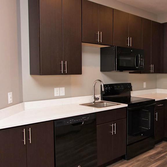 Thumbnail 3 of 7 A kitchen with brown cabinets and black appliances.