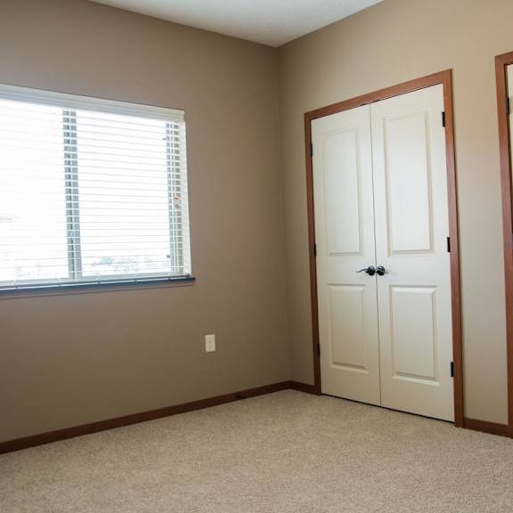 Thumbnail 8 of 13 A room with a window, carpet, and 2 sets of double closet doors