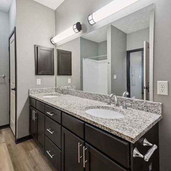 Thumbnail 21 of 33 A bathroom with a double sink granite vanity, dark cabinets, oversized mirror with overhead lighting and a medicine cabinet.