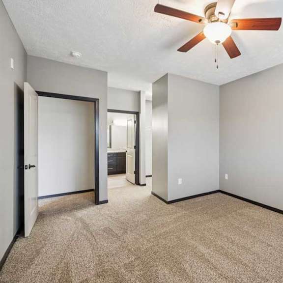 Thumbnail 18 of 33 A carpeted bedroom with a ceiling fan, walk-in closet, and attached bathroom.