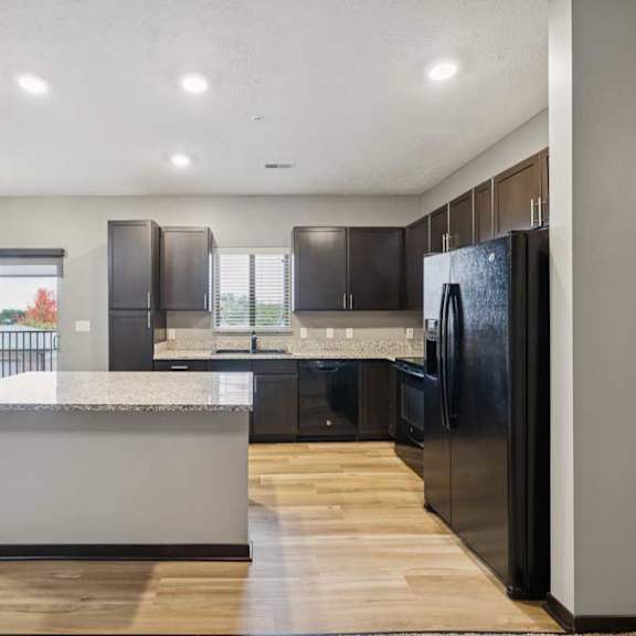 Thumbnail 8 of 33 A kitchen with dark cabinets, granite countertops, black appliances, a window over the sink, and a large island.