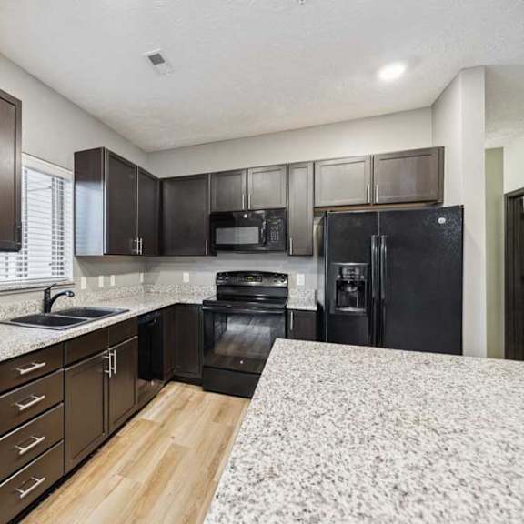 Thumbnail 11 of 33 A kitchen with dark cabinets, granite counters, and black appliances.