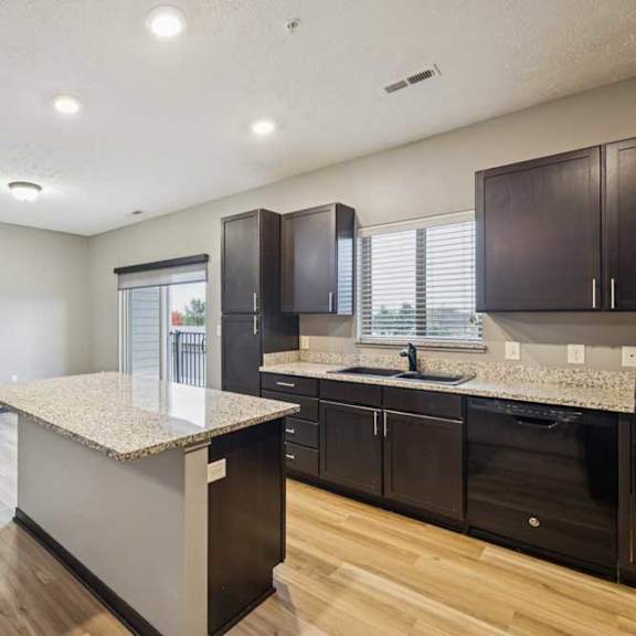 Thumbnail 9 of 33 A kitchen with dark cabinets, granite counters, a large island, open to a dining room with a sliding glass door to a balcony.