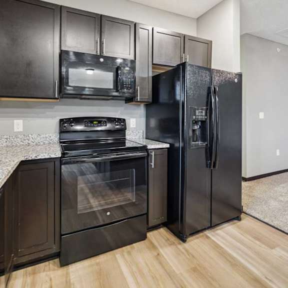 Thumbnail 12 of 33 A close up of a black range and microwave in a modern kitchen with dark cabinets and light granite countertops.