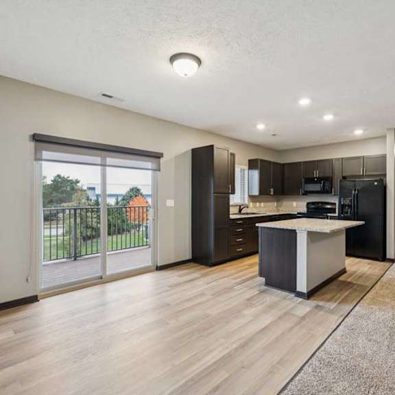 Thumbnail 14 of 33 A dining area with a sliding glass door to a balcony, next to a modern kitchen with dark cabinets and granite countertops.