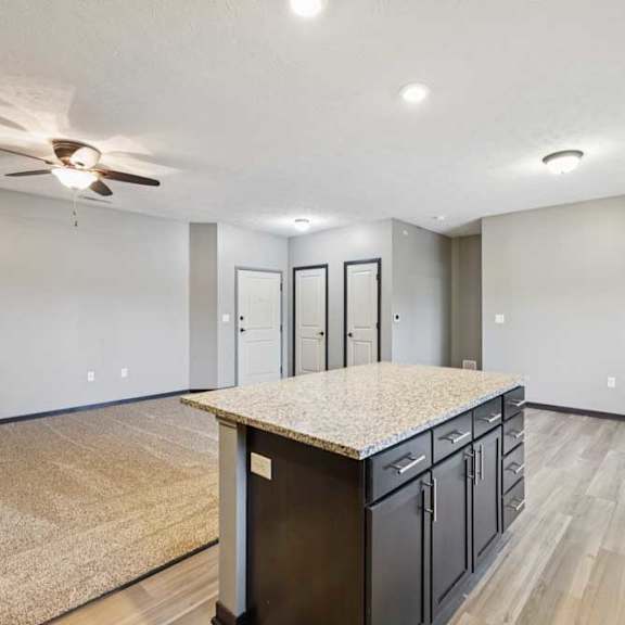 Thumbnail 10 of 33 A kitchen island with dark cabinets in front of an open, carpeted living room.