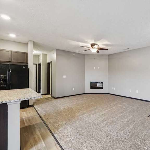 Thumbnail 4 of 33 A spacious, carpeted living room with an electric fireplace and a ceiling fan.