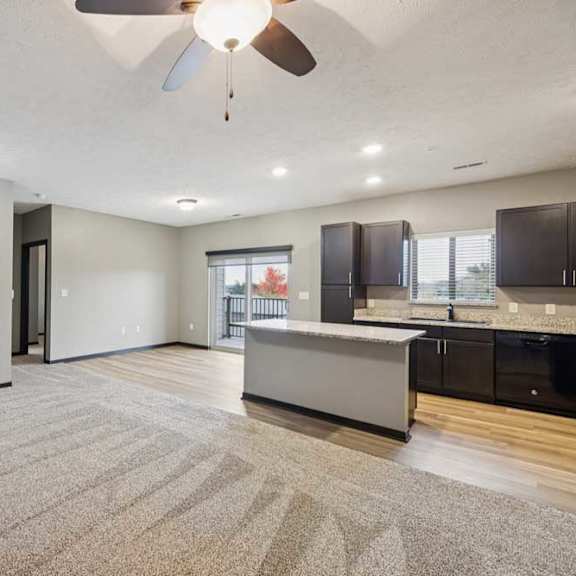 Thumbnail 5 of 33 A spacious living room with carpeted flooring, open to a kitchen with a large island.