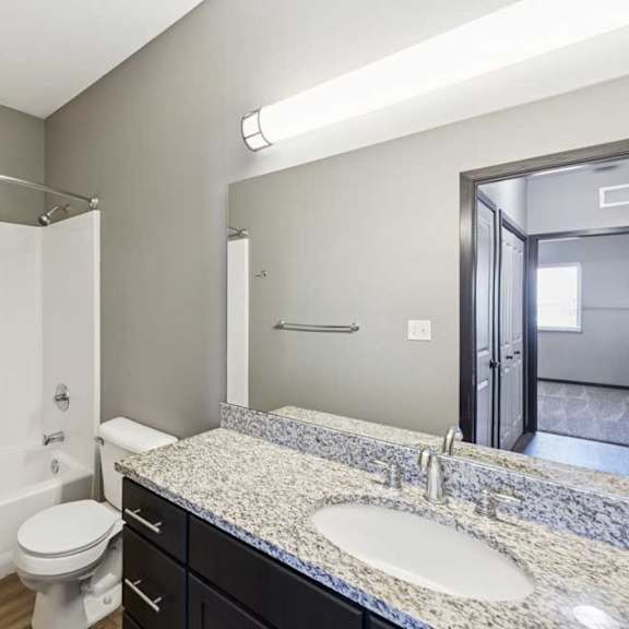 Thumbnail 22 of 30 Bathroom with tub and shower combo, granite-look vanity, dark cabinetry, and large mirror.