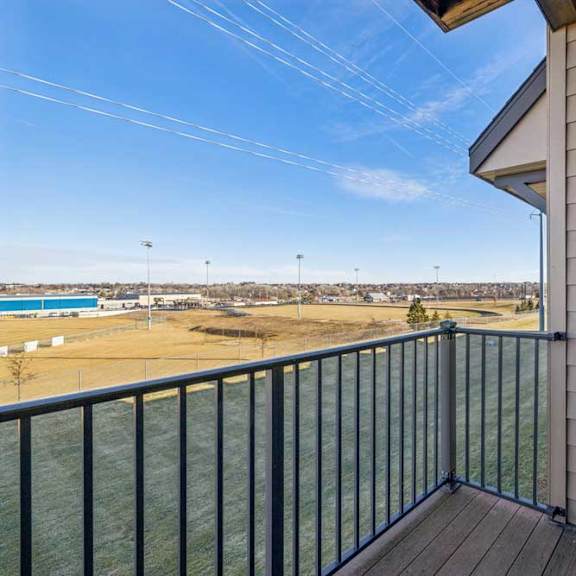 Thumbnail 13 of 30 Private apartment balcony with wood-style flooring and metal railing overlooking open green space and nearby buildings.