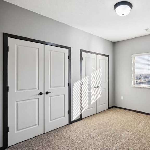 Thumbnail 12 of 23 A room with a carpeted floor, two doors, and a window with blinds.