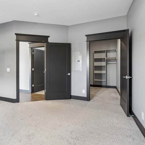 Thumbnail 32 of 46 Carpeted apartment bedroom with gray walls, bold dark trim, and direct access to a walk-in closet with built-in shelving.