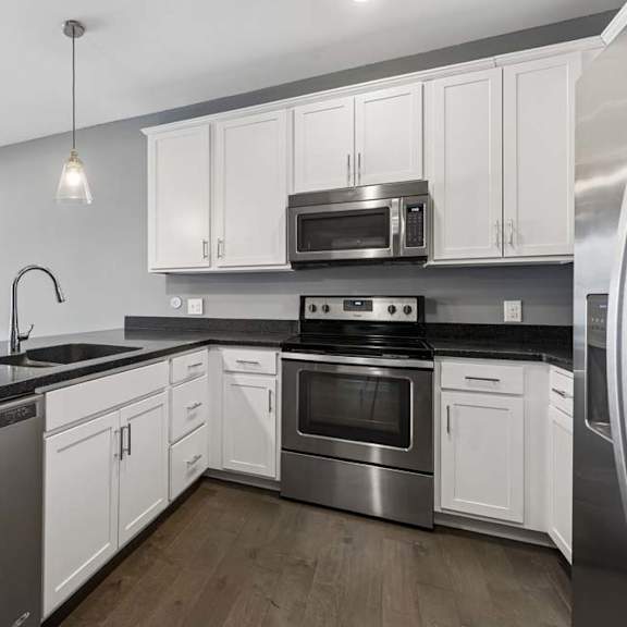 Thumbnail 24 of 46 White cabinetry and dark countertops frame this apartment kitchen, complete with stainless steel appliances, pendant lights, and a peninsula sink.