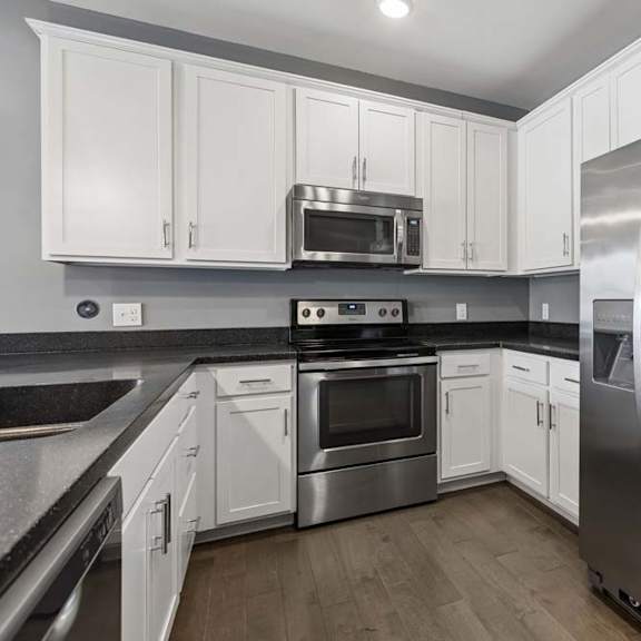 Thumbnail 25 of 46 Stainless steel refrigerator, oven, and microwave stand out against crisp white cabinets and dark counters in this apartment kitchen.