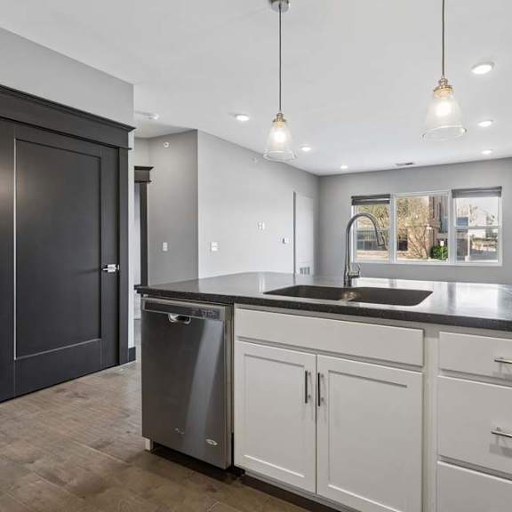 Thumbnail 26 of 46 Long kitchen peninsula with an undermount sink, white cabinetry, dark countertop, pendant lighting, and an open view into the living area.