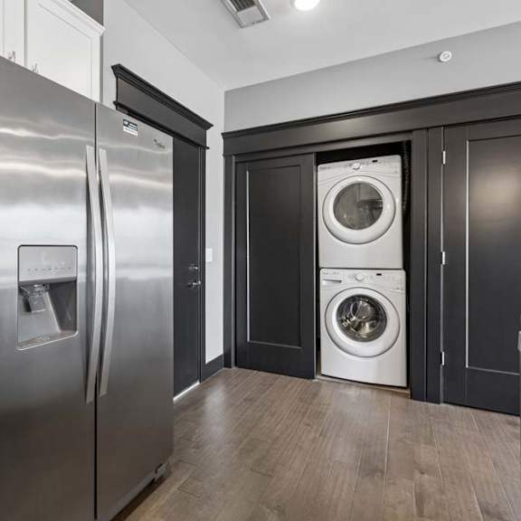 Thumbnail 28 of 46 In-home laundry is tucked beside the apartment kitchen, with a stacked washer and dryer framed by dark doors and trim.