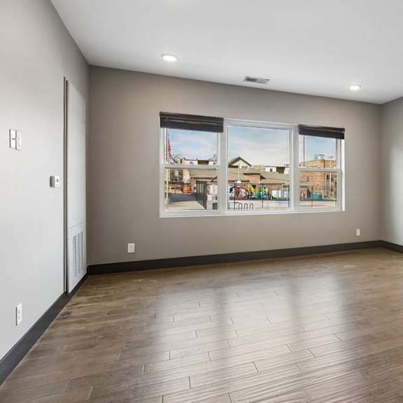 Thumbnail 29 of 46 Wide windows fill this open apartment living room with natural light, complemented by gray walls, dark trim, and wood-look flooring.