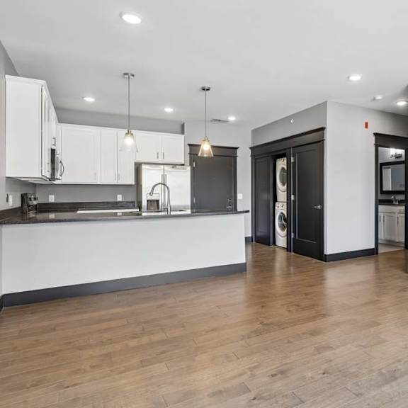 Thumbnail 30 of 46 Open living space connects to a white-cabinet kitchen and tucked-away laundry area, finished with wood-look floors and dark trim.