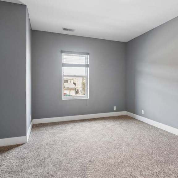 Thumbnail 43 of 46 Soft natural light enters this unfurnished apartment bedroom, highlighting gray walls, neutral carpeting, and crisp white trim.