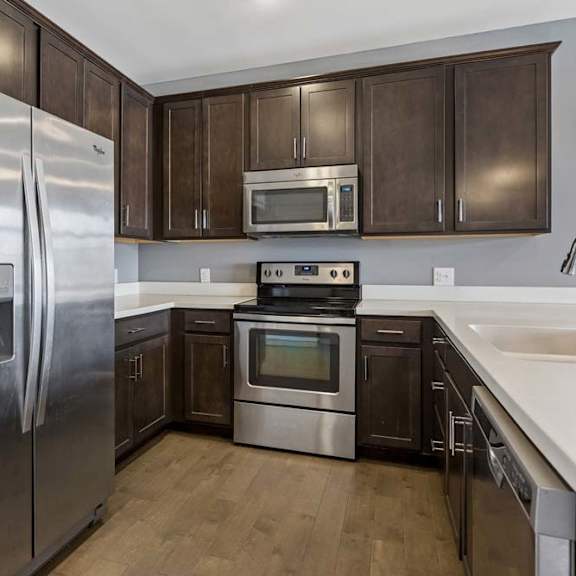 Thumbnail 36 of 46 Dark wood cabinetry wraps around this apartment kitchen, paired with white counters, stainless steel appliances, and a peninsula sink.