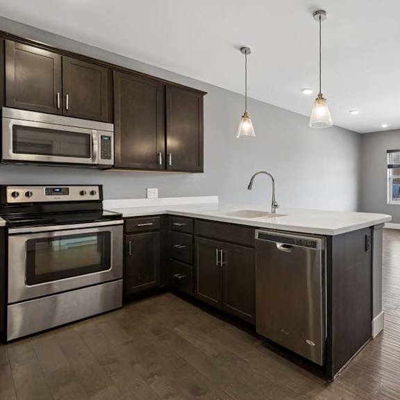 Thumbnail 37 of 46 Dark cabinetry and a white peninsula define this open apartment kitchen, flowing into a living area with wide windows and wood-look floors.